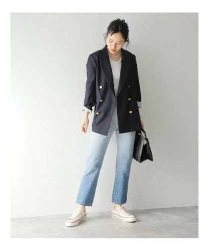 日本女性穿深色雙排扣西裝外套、白色 T 恤、淺藍直筒牛仔褲、白色球鞋並提黑色手提包