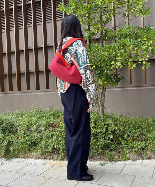 日本品牌穿搭街拍:亞洲女性背向鏡頭,穿多色圖案襯衫、藏青寬褲、黑鞋並背紅色肩背包
