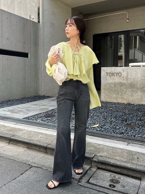 日本女性穿淺黃綠荷葉上衣、炭灰喇叭牛仔褲與黑色平底涼鞋,手提白色托特包