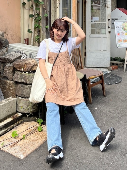 日本女性穿白色 T 恤、粉色蕾絲吊帶洋裝,搭配淺藍寬牛仔褲、白色托特包與黑色球鞋