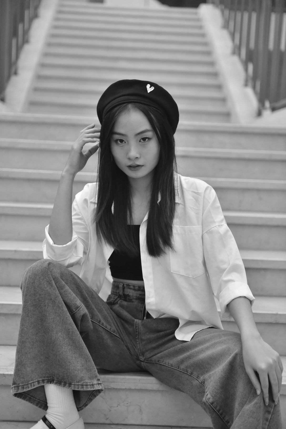 亞洲女性坐在階梯上,穿白色襯衫、黑色內搭與灰色寬版牛仔褲