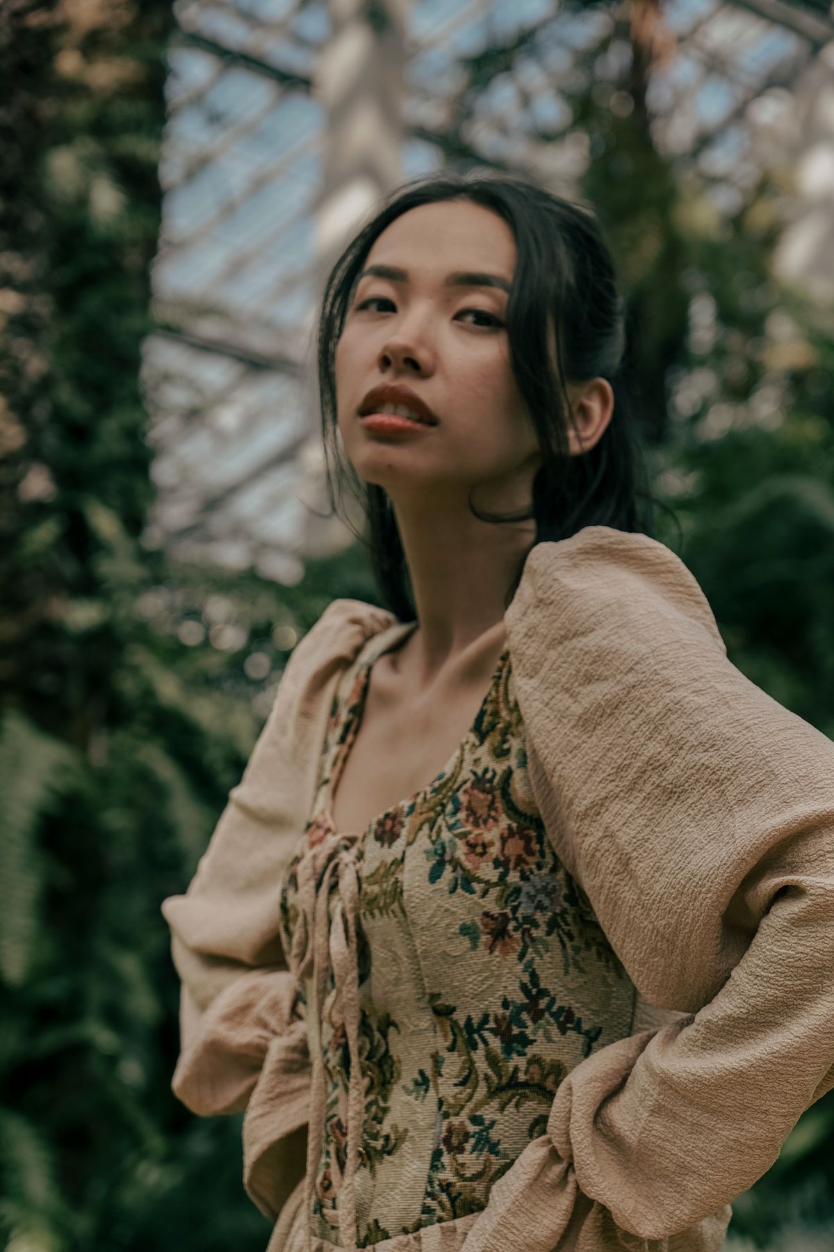 亞洲女性穿米色針織外搭與植物印花連身裙,站在綠植環境中
