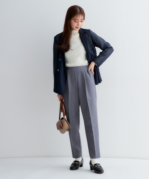 亞洲女性穿藏青西裝外套、白色針織上衣、灰色西裝長褲與黑色樂福鞋