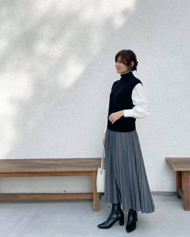 亞洲女性穿黑色針織背心、白色泡袖襯衫、灰色百褶中裙與黑色短靴