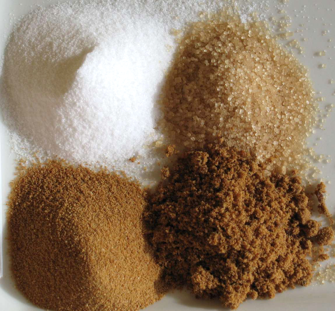 白色精製糖與幾種較深色糖樣品並排，呈現晶粒大小與顏色差異