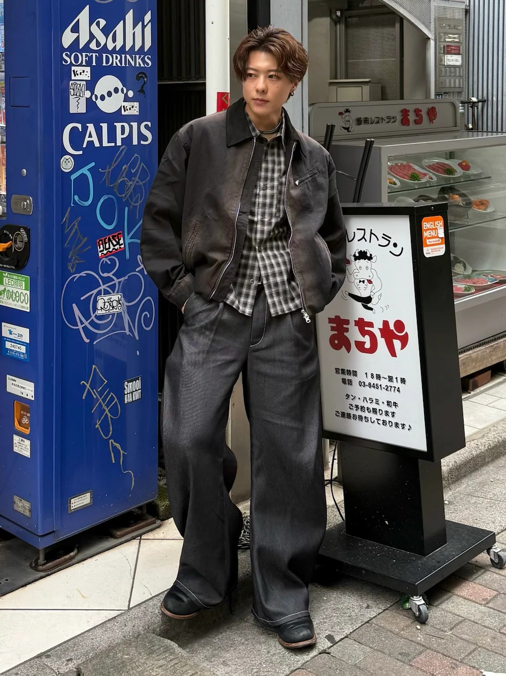 日本男性穿黑色短外套與黑灰格紋襯衫,搭配黑色側摺弧形寬丹寧褲及黑色皮靴