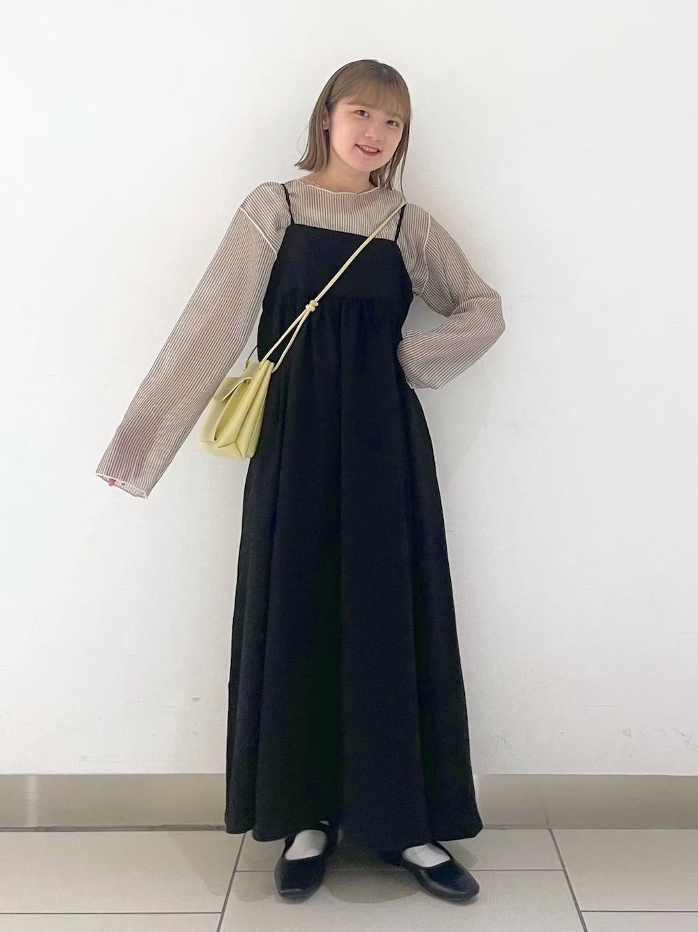 日本女性穿透膚條紋長袖上衣、黑色細肩帶洋裝、黑色平底繫帶鞋並背淺黃色小包