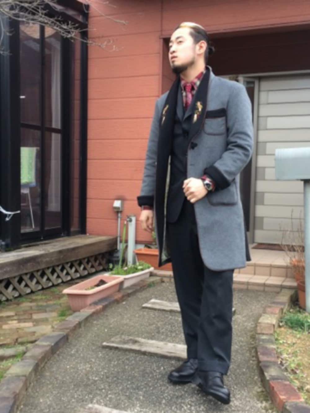 男士穿深色西裝背心與紅色系襯衫領帶，外搭灰色長大衣，展示正式服裝的層次組合