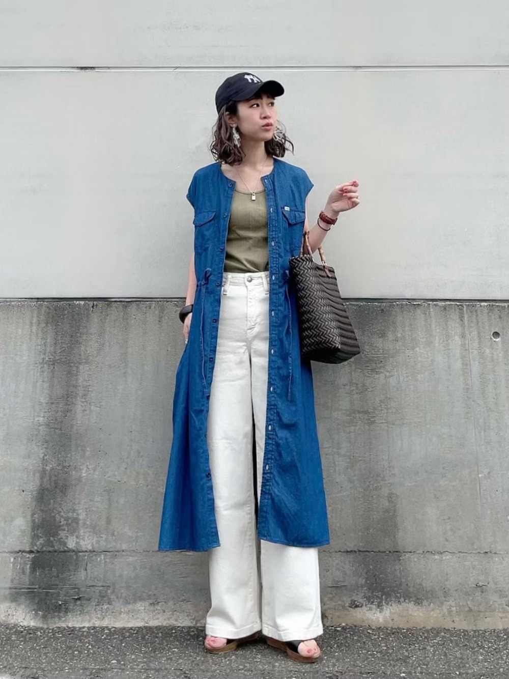 日本 WEAR 實穿:藍色無袖牛仔襯衫洋裝敞開穿在橄欖綠背心外,搭配白色寬褲、涼鞋、深色托特包與帽子