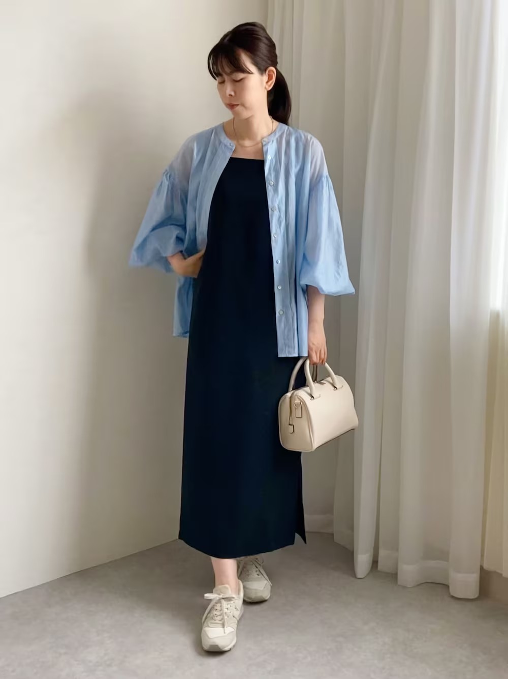 日本 WEAR 實穿:藍色輕薄罩衫敞開穿在深色長洋裝外,搭配白色手提包與休閒球鞋