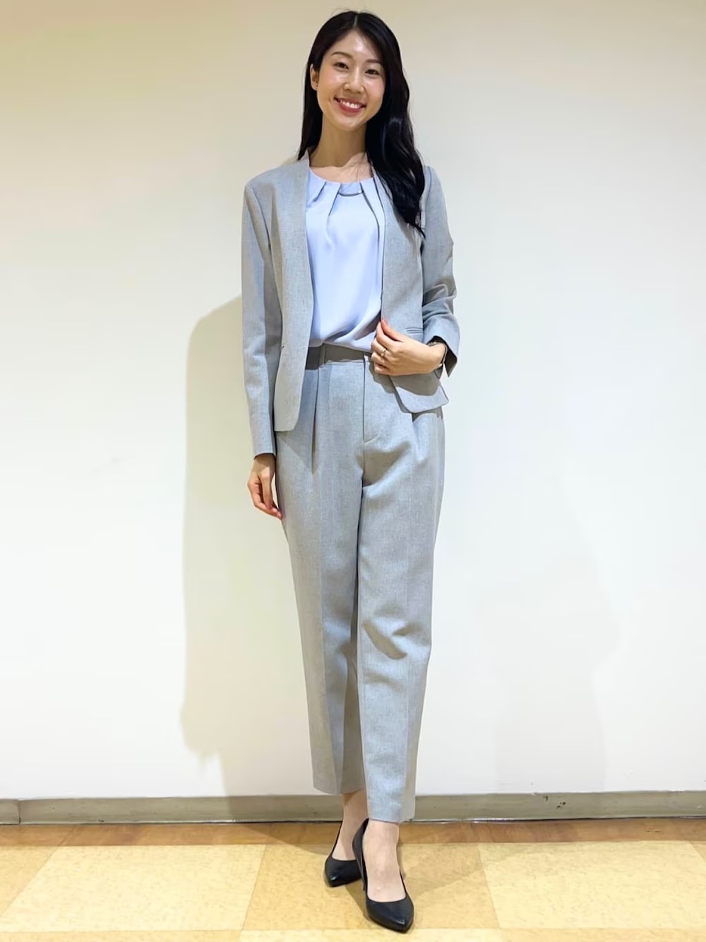 日本女性穿淺灰無領西裝外套與同色錐形褲、淡藍襯衫及黑色尖頭跟鞋的通勤造型