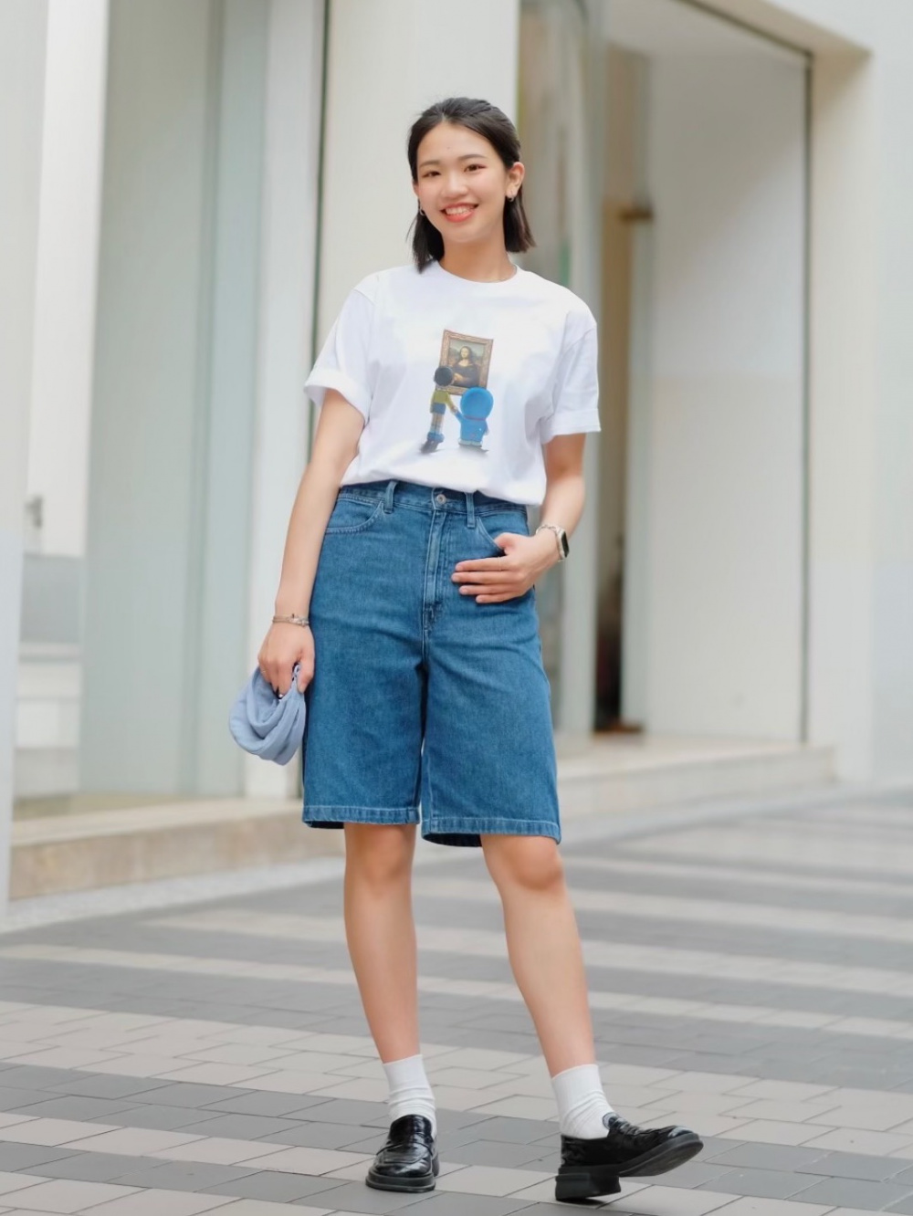亞洲女性穿白色圖案 T、丹寧百慕達短褲、白襪與黑色樂福鞋